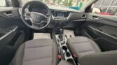 Interior of a Hyundai sedan: steering wheel, dashboard with center display, climate controls, gear shifter, and front two cloth seats with cupholders between them.