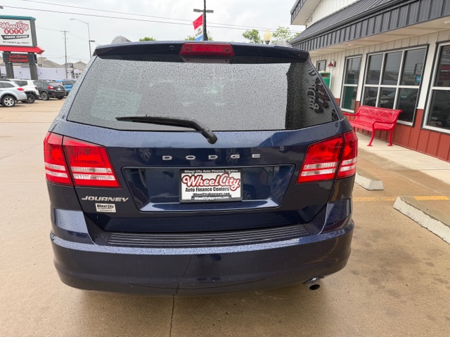 Rear view of a blue Dodge Journey SUV in a dealership lot, with a Wheel City license plate frame and a wet rear window.