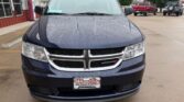 Front view of a dark blue Dodge minivan at a dealership lot on a rainy day, with raindrops on the hood and windshield.
