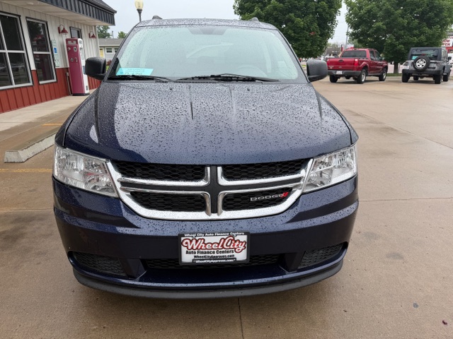Front view of a dark blue Dodge minivan at a dealership lot on a rainy day, with raindrops on the hood and windshield.