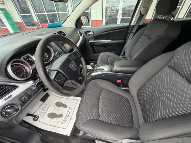 Front interior of a car showing the steering wheel, dashboard, and two gray fabric seats.