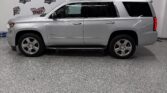 Side view of a silver Chevrolet Tahoe SUV parked indoors, with a Wheel City Auto Finance Centers banner in the background.
