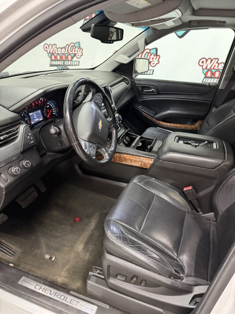 Front interior of a Chevrolet SUV showing black leather seats, steering wheel, center console, and wood-trim dashboard accents.