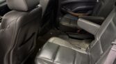 Interior of a black leather-lined SUV cabin, rear seats folded upright with visible seat belts and wood trim on door panel