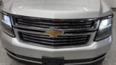 Front view of a silver Chevrolet SUV in a dealership showroom, with headlights on and a chrome grille featuring the gold bowtie emblem.