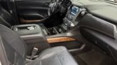 Front interior of a black Chevrolet SUV showing the driver’s seat, steering wheel, center console, and wood trim accents in a showroom setting.