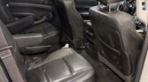 Rear passenger interior of a black leather SUV with two captain chairs and front seats visible through the open door (dark upholstery, wood trim)