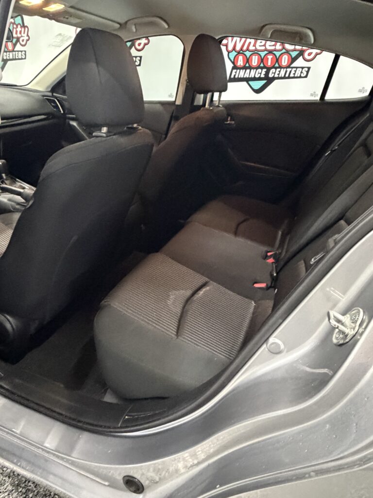 Interior of a car's back seat area with black fabric seats, two headrests, and visible seat belts; photo taken from the open rear passenger door.