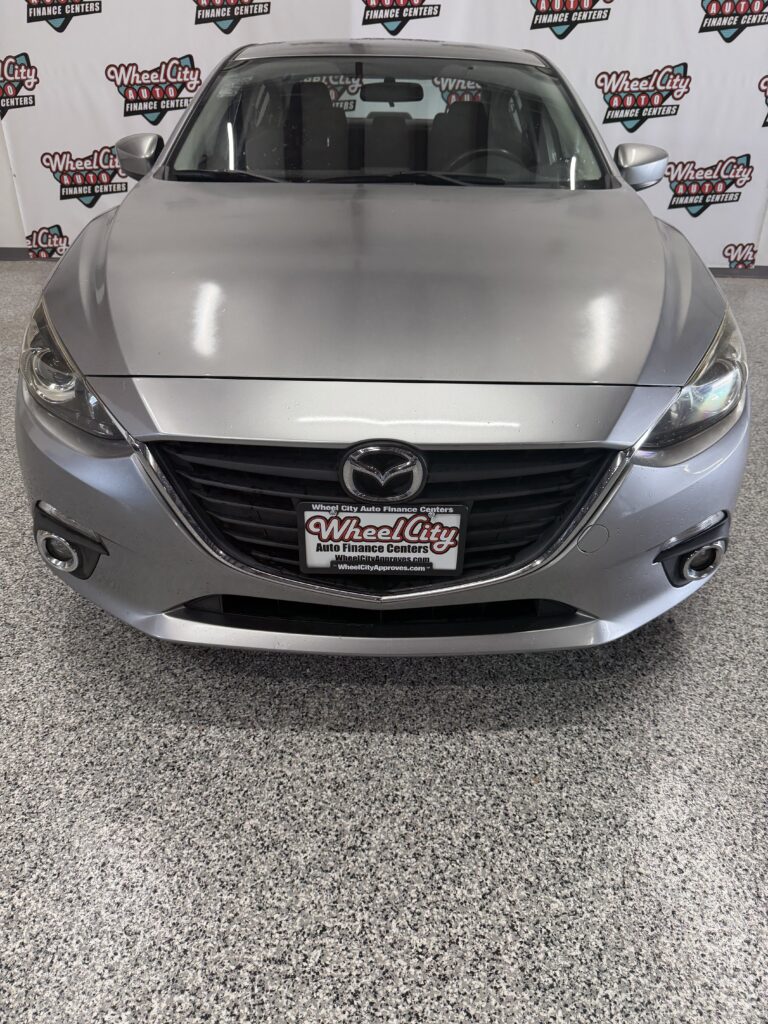 Front view of a silver Mazda car in a dealership showroom with Wheel City Auto Financing Centers backdrop