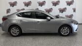 Side view of a silver four-door sedan parked indoors in front of a white backdrop with Wheel City Auto Finance Centers logos.