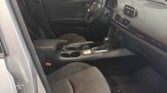 Interior of a Mazda3 showing the front seats, steering wheel, center console, and dashboard viewed from the open driver's side door.