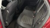 Rear passenger seating in a black fabric car interior, back seat with visible headrests and seat belts; red car door frame visible.