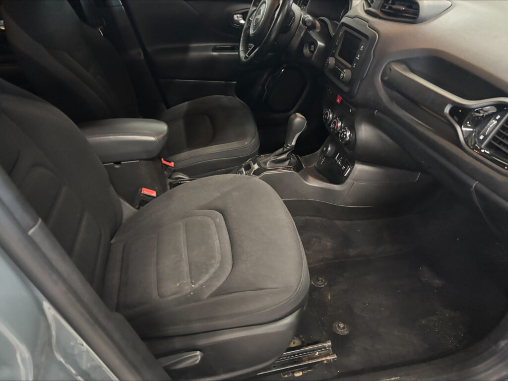 Front interior of a dark car: driver and passenger seats with center console and gear shifter visible on the floor left of the passenger seat inside a black cabin.