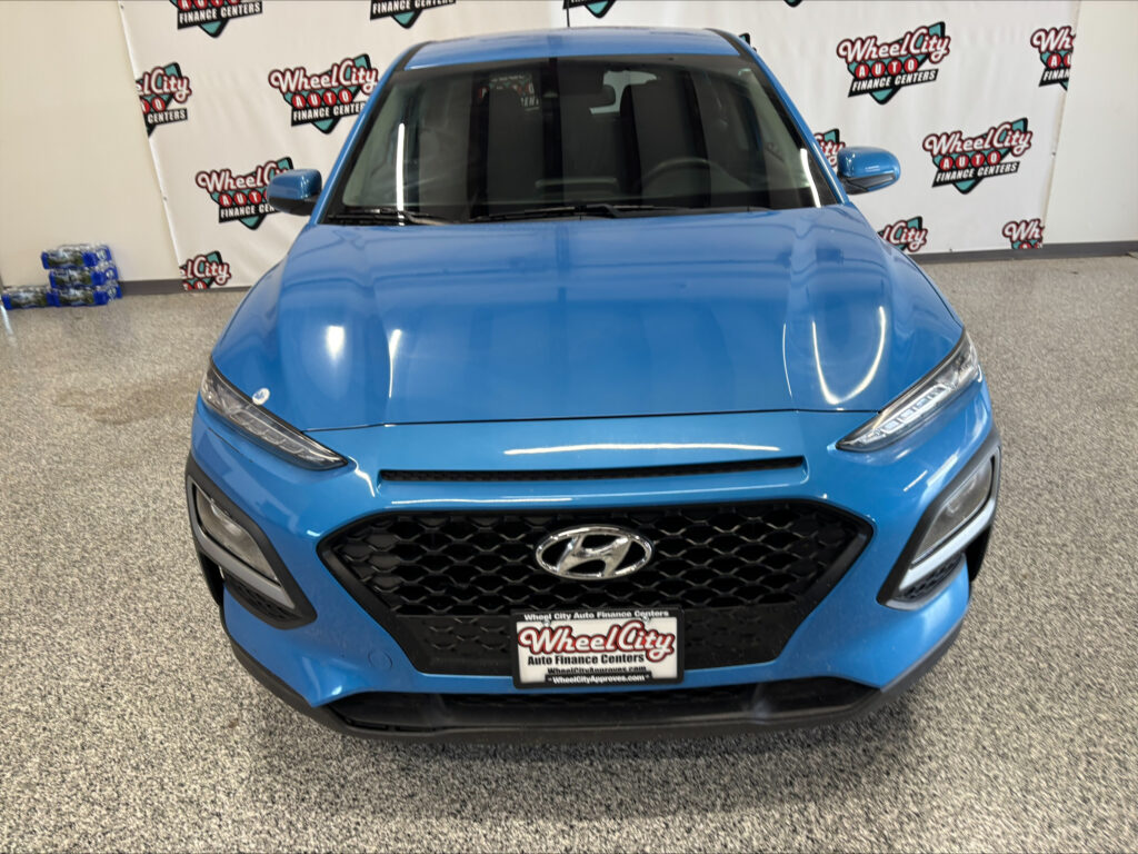 Front view of a blue Hyundai SUV in a showroom with branded backdrop reading Wheel City Auto Finance Centers.