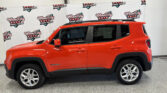 Red Jeep Grand Cherokee SUV parked indoors beside a branded backdrop reading Wheel City Auto Finance Centers, with visible roof rails and alloy wheels.