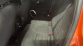 Back seat of a car with dark gray fabric seats, visible seat belts, and a door panel; orange car frame visible on the right edge.