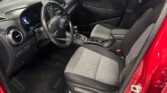 Interior of a modern car cabin: driver's seat, steering wheel, center touchscreen, and front passenger seat visible in a red vehicle door frame