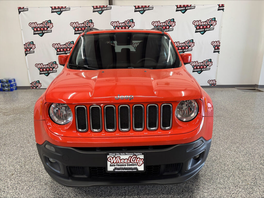 Front view of a red Jeep SUV in a showroom with Wheel City Auto Finance Centers banners in the background.
