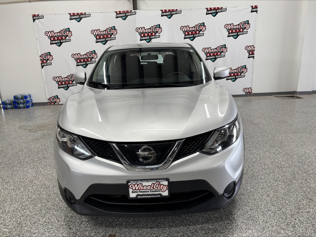 Front view of a silver Nissan SUV indoors, with a Wheel City Auto Finance Centers backdrop behind it.