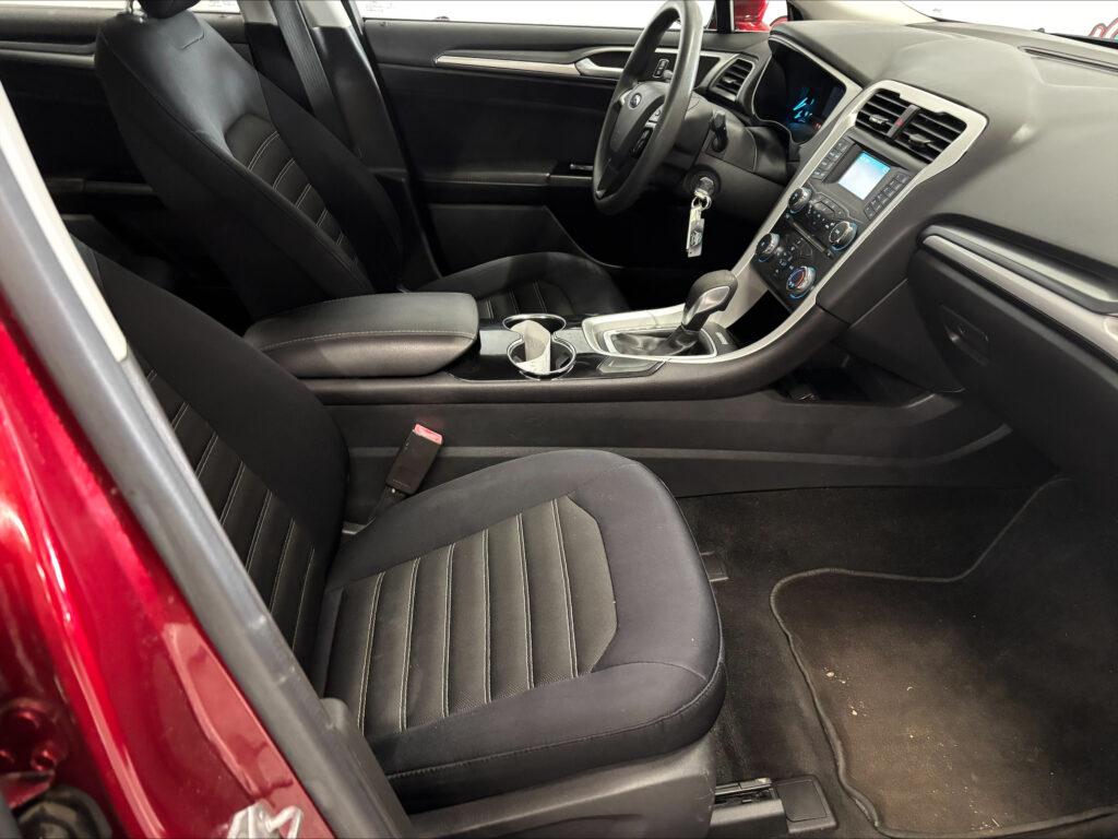 Front interior of a red car showing black leather seats, center console, and dashboard with gear shifter and steering wheel visible.
