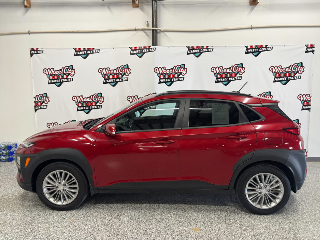 Red SUV indoors in front of a Wheel City Auto Finance Centers backdrop banner.
