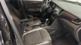 Interior view of a black leather car cabin with the steering wheel, center console, and touchscreen display visible; dealership signage seen through the windows in the background.