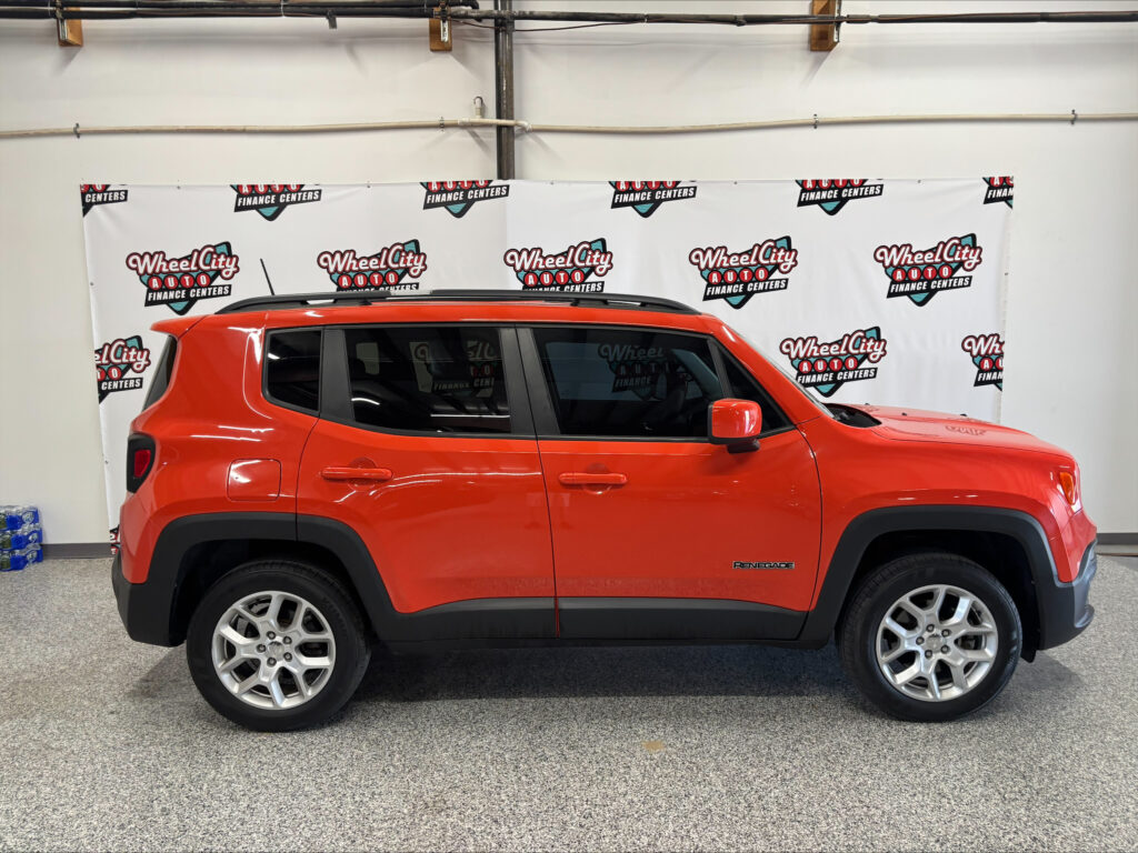 Red Jeep Renegade with roof rails parked indoors in front of a banner reading Wheel City Auto Finance Centers.
