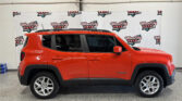 Red Jeep Renegade with roof rails parked indoors in front of a banner reading Wheel City Auto Finance Centers.