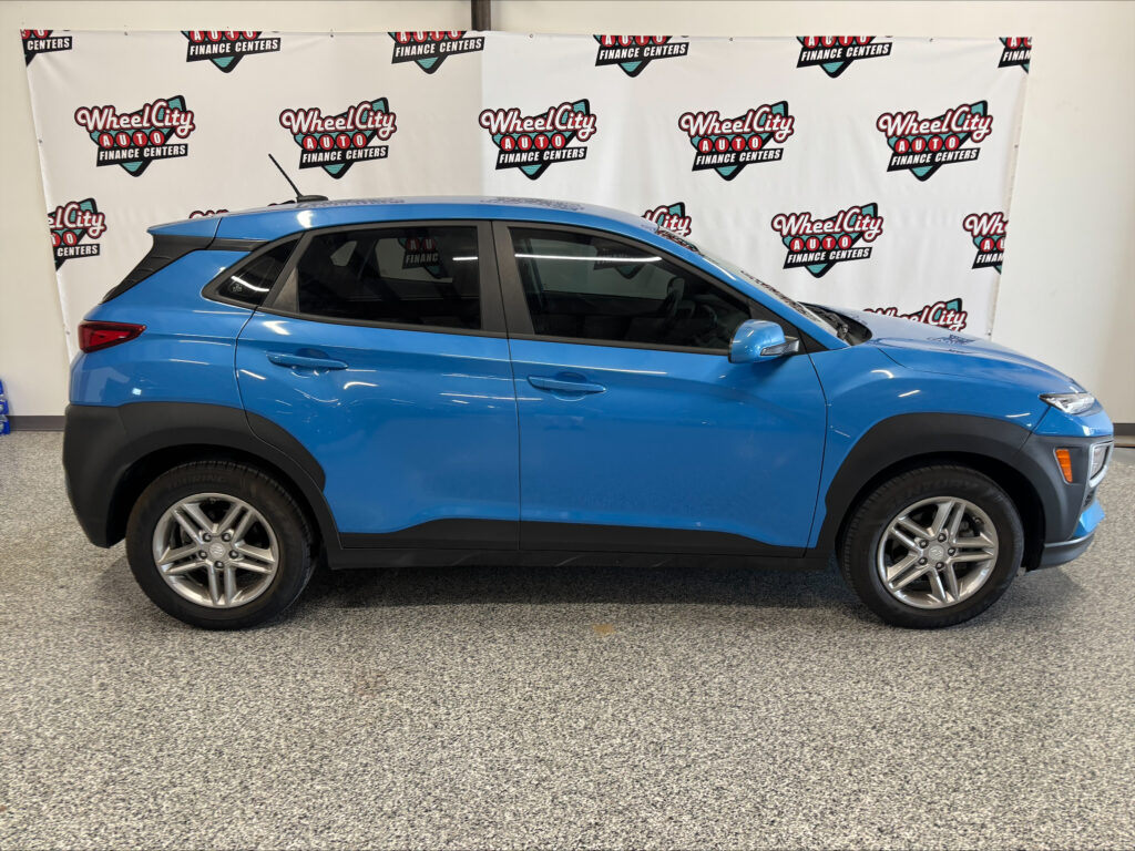 Blue SUV parked indoors in front of a Wheel City Auto Finance Centers banner backdrop on a showroom wall.