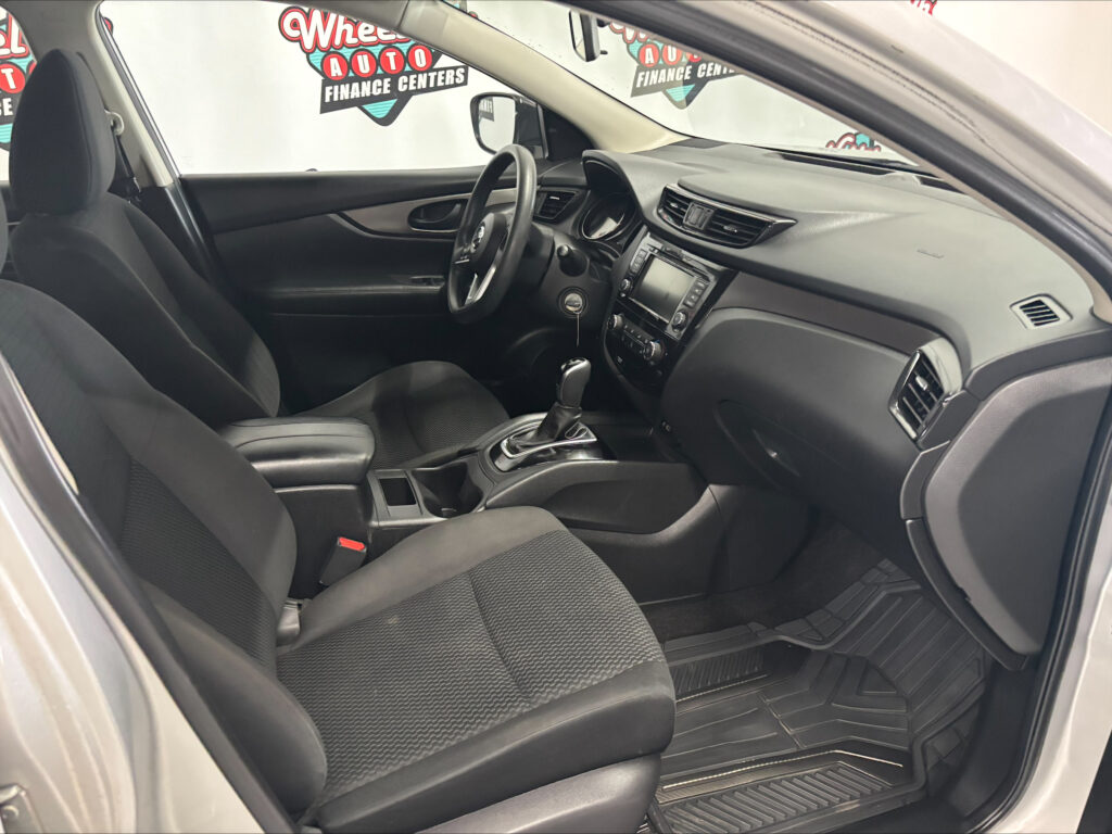 Interior of a sedan showing the front seats, steering wheel, center console with a touchscreen, and floor mats, all in dark fabric upholstery.