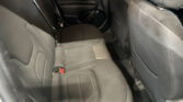 Rear passenger seating area in a dark fabric car interior, with visible seat belts and door panel.