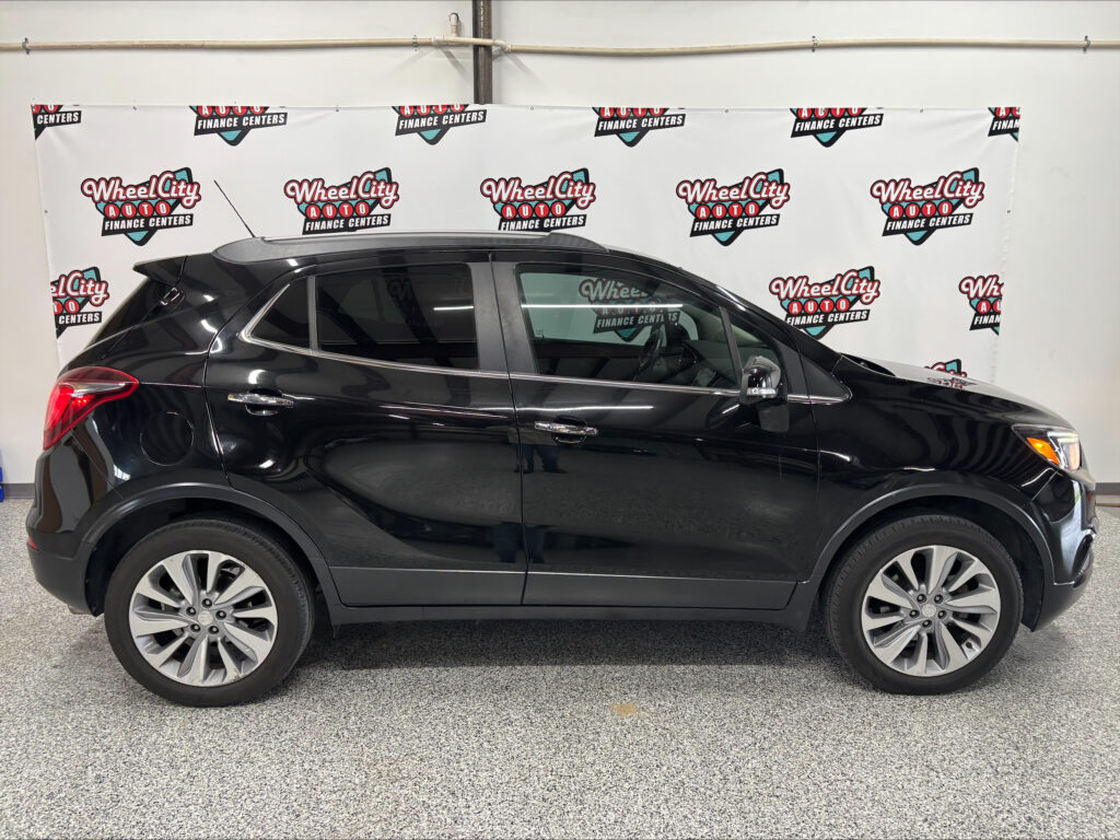 Side view of a black SUV parked indoors with a Wheel City Auto backdrop in the background showing logos and branding.