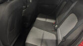 Back seat of a car with black-and-white checkered fabric, visible seat belts and door panel, red car exterior visible at edge.
