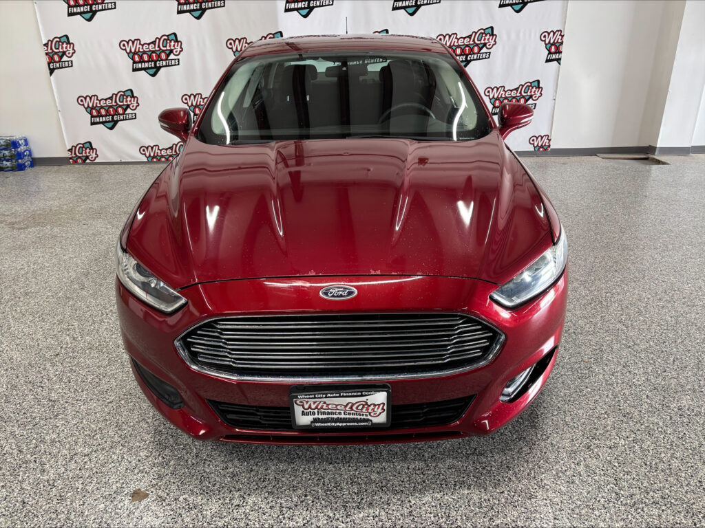 Front view of a red Ford car in a showroom with Wheel City Auto Finance Centers backdrop behind it.