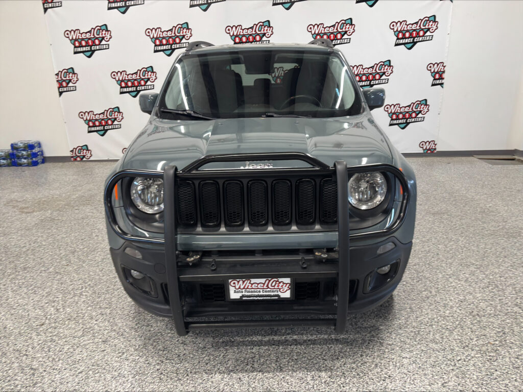 Front view of a gray Jeep Wrangler in a showroom, with a Wheel City Auto Finance Centers backdrop behind it.