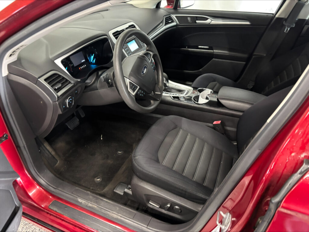Interior of a red car showing the driver’s seat, steering wheel, and center console with a digital display screen.