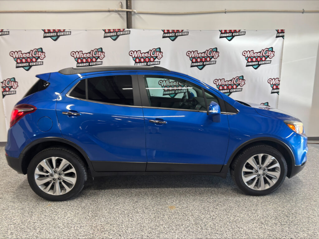 Blue SUV parked indoors in front of a Wheel City Auto Finance Centers banner backdrop; side profile with chrome trim and large alloy wheels.