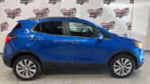 Blue SUV parked indoors in front of a Wheel City Auto Finance Centers banner backdrop; side profile with chrome trim and large alloy wheels.