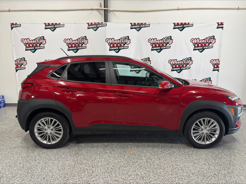 Red SUV parked indoors in front of a white banner with Wheel City Auto Finance Centers logos.