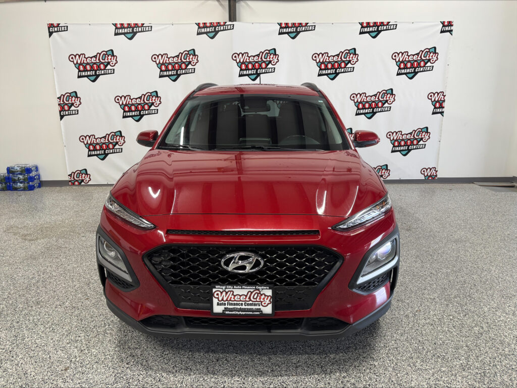 Front view of a red SUV inside a showroom, with a 'Wheel City Auto Finance Centers' backdrop.