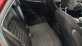 Passenger-side view of a car's black fabric back seat with vertical stitching and red seat belt buckles; door panel and front seats visible.