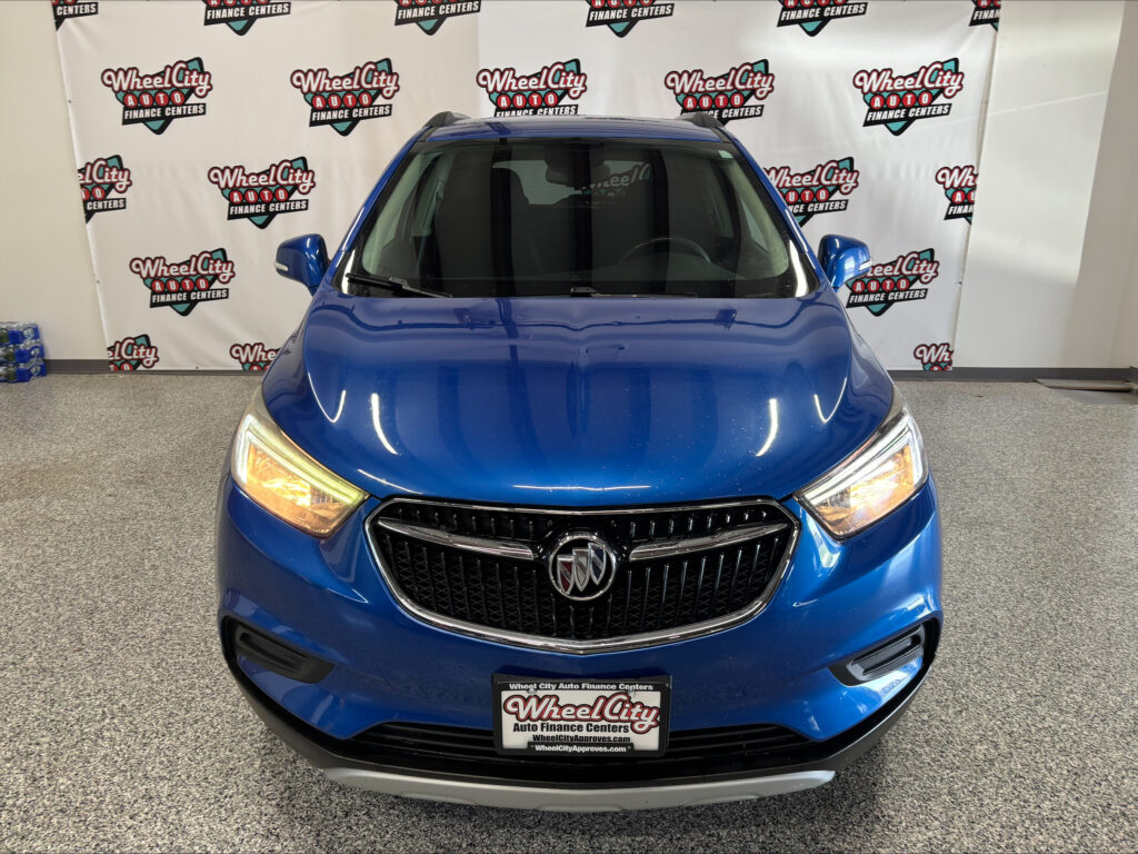 Front view of a blue Buick SUV in a showroom with a Wheel City Auto Finance Centers backdrop and license-plate frame.