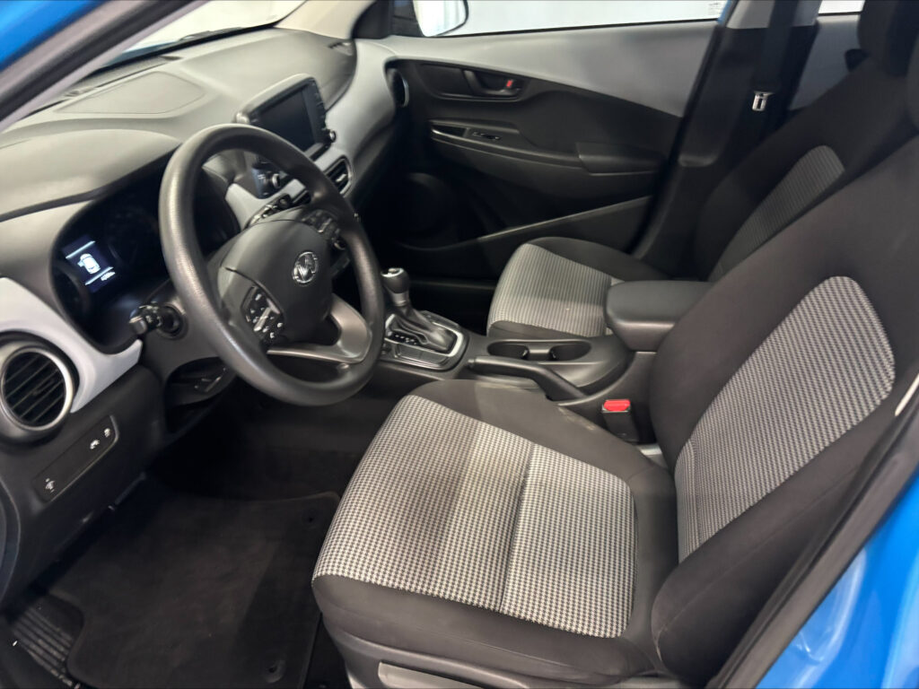 Interior view of a car's front cabin: steering wheel, dashboard, center console, and gray checkered seats with a gear shifter visible