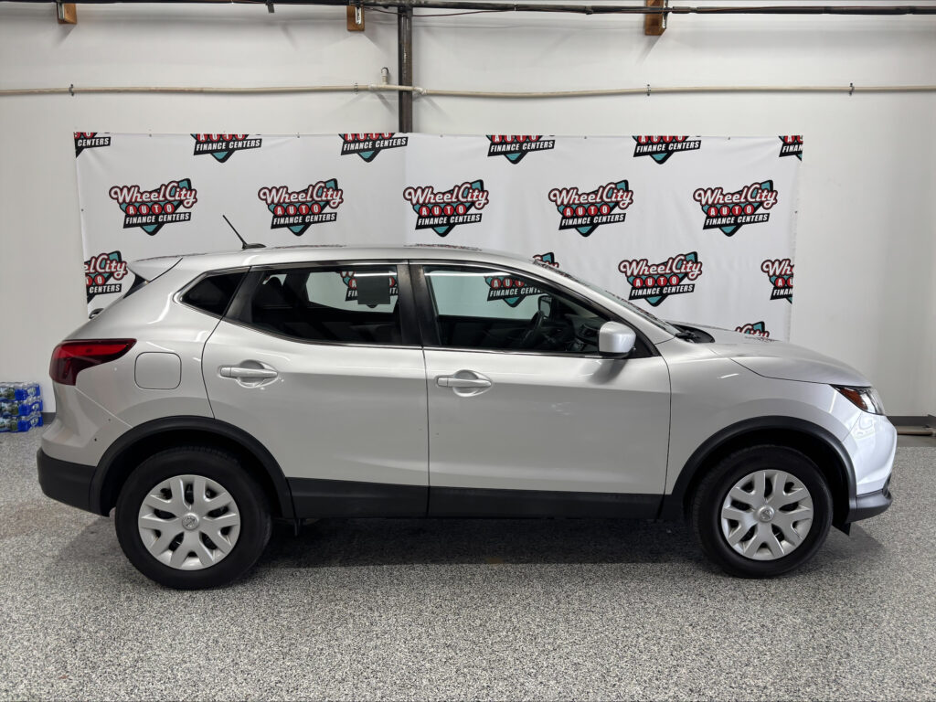 Side view of a silver SUV inside a showroom with Wheel City Auto Finance Centers banners in the background.