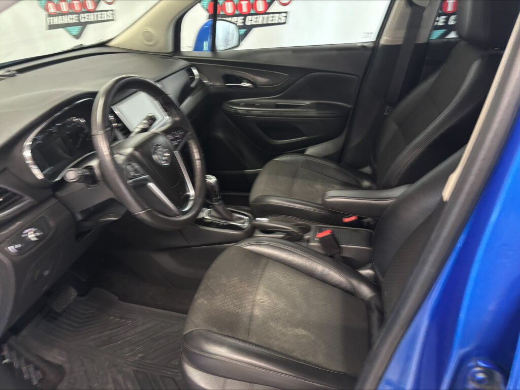 Interior of a blue car showing the driver's seat, steering wheel, center console, and front passenger seat with black upholstery from the open door side view.