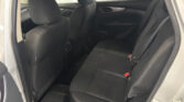 Interior of a car's rear seat area, showing black fabric seats, the back of the front seats, and a door panel with a window displaying advertisements outside.