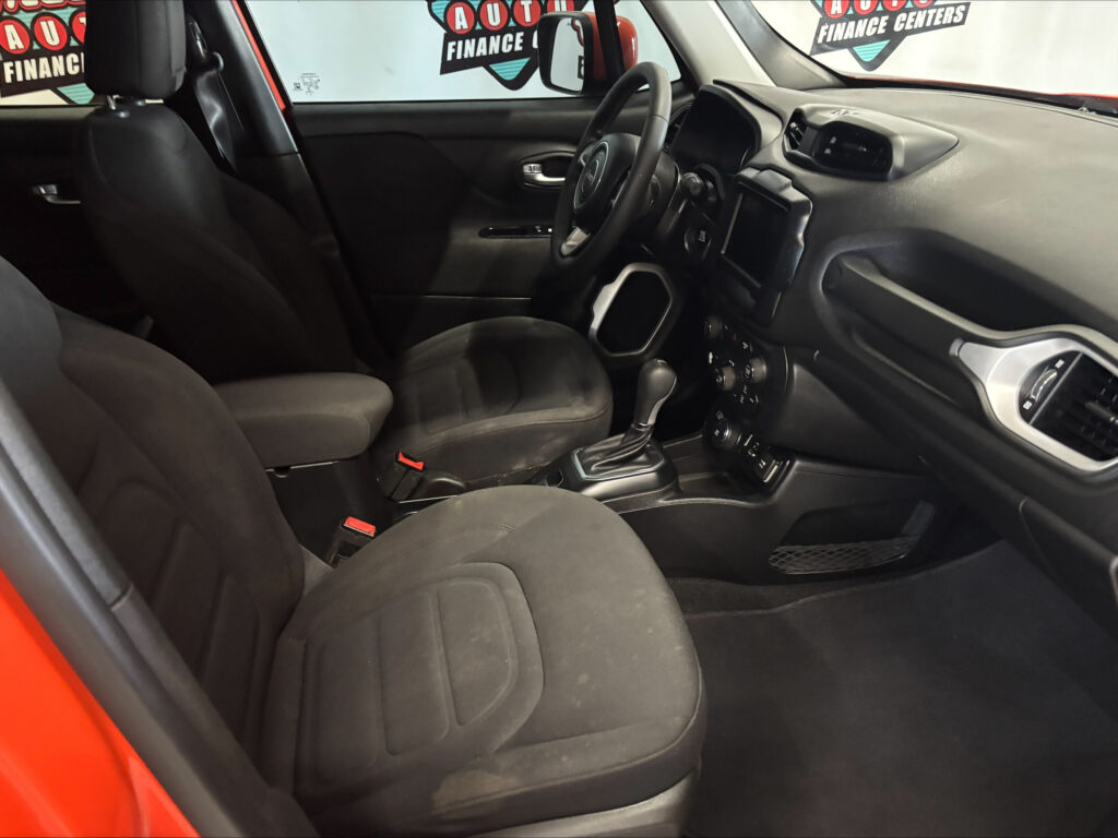 Front interior of a car with black fabric seats, steering wheel, center console, and dashboard viewed from the passenger side door open edge.