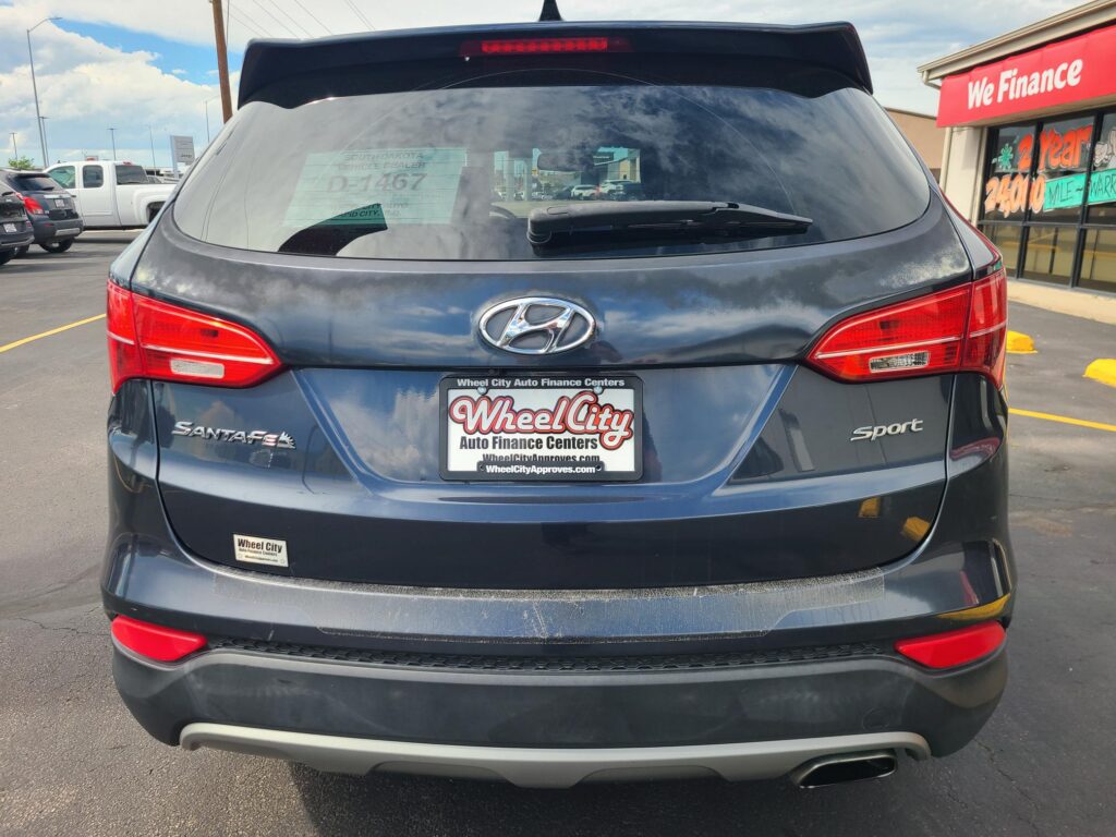 Rear view of a dark gray Hyundai Santa Fe Sport in a dealership lot with Wheel City license plate frame visible and a 'We Finance' sign in the background.
