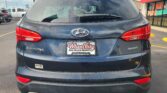 Rear view of a dark gray Hyundai Santa Fe Sport in a dealership lot with Wheel City license plate frame visible and a 'We Finance' sign in the background.