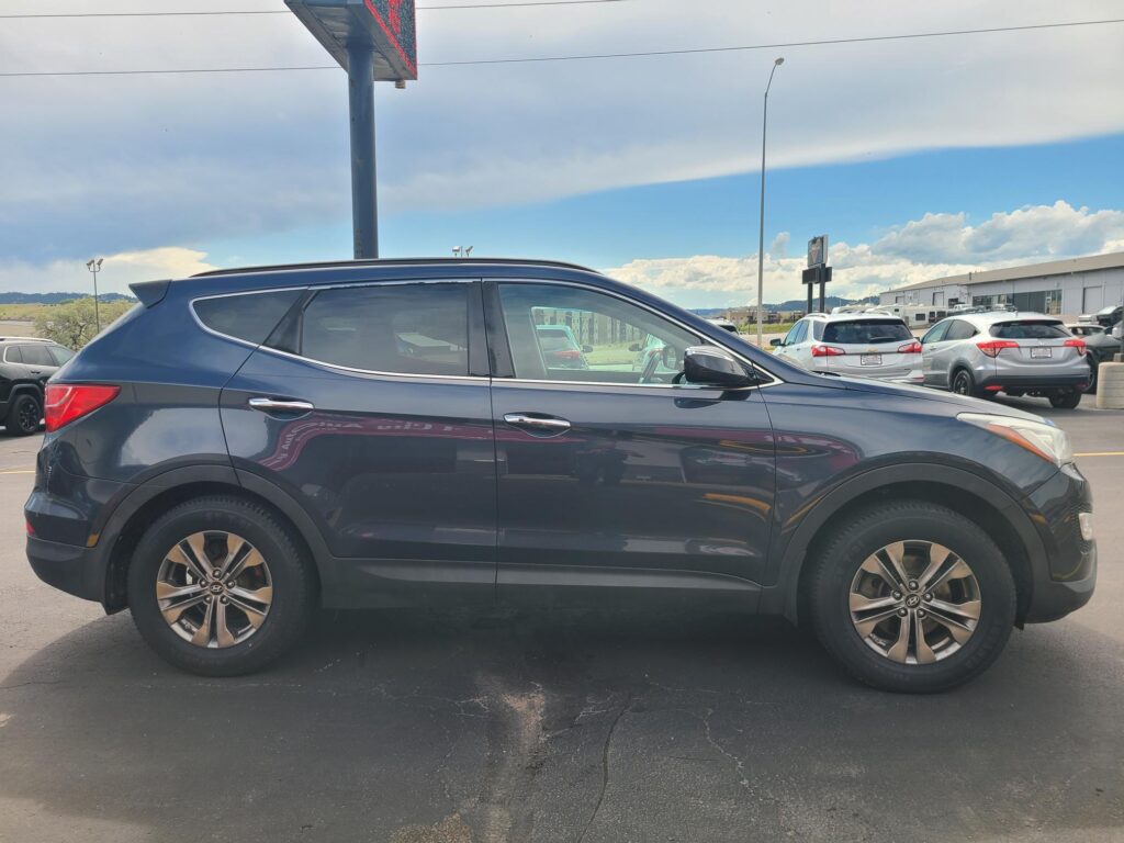 Side view of a dark blue SUV parked in a lot, with other cars and an industrial building in the background under a cloudy sky